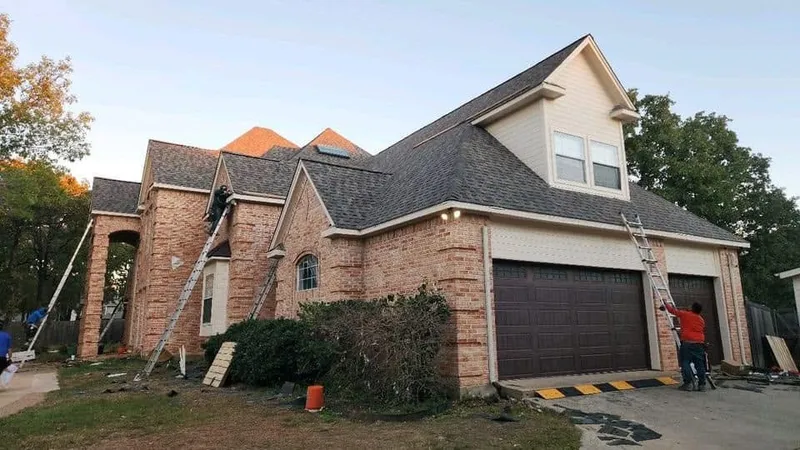 Roofers on ladders at a brick home with a new dark shingle roof
