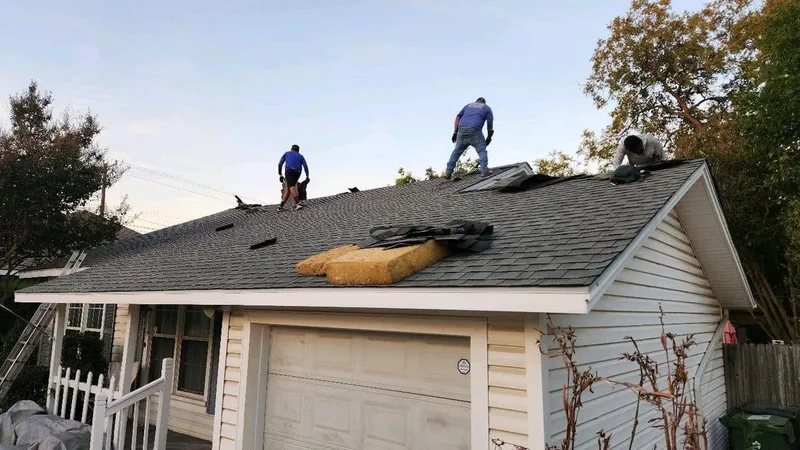 Roofers working on the shingle roof of a one-story home