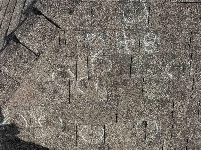 Hail hits circled in chalk on a shingle roof during an inspection