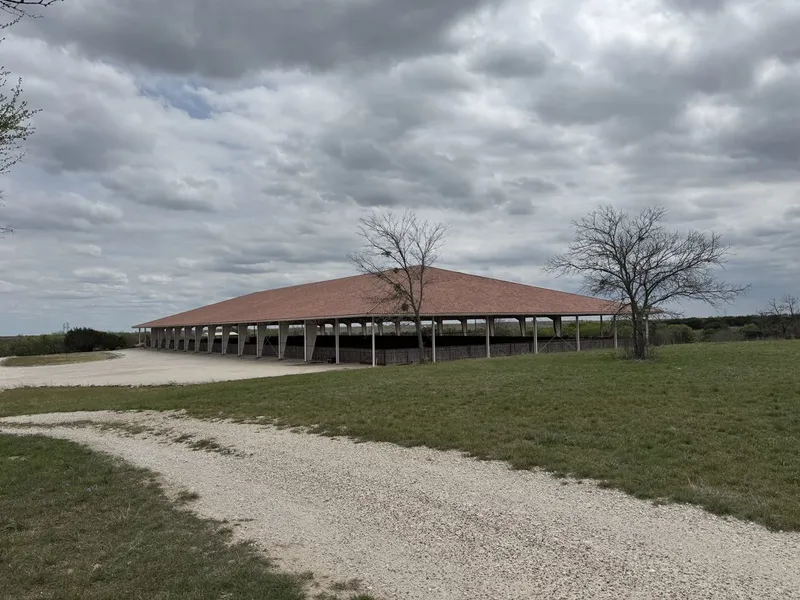 A long open-sided pavilion with a red roof on a ranch property