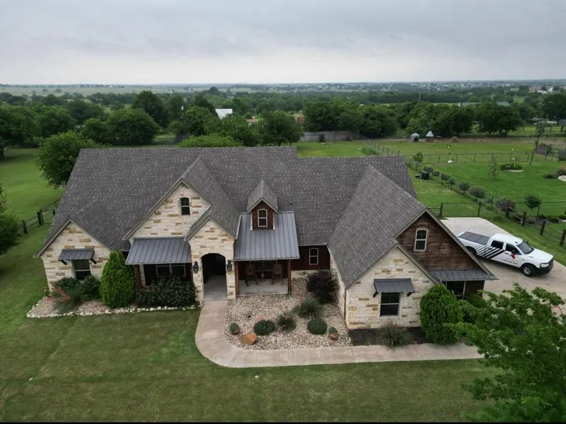 A stone ranch home with a shingle roof and metal porch roofs, seen from above