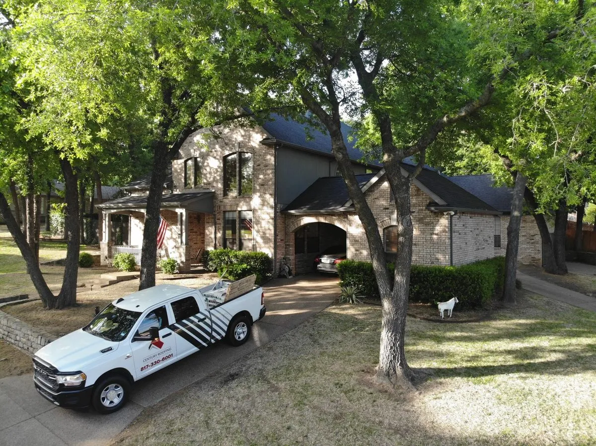 A Century Roofing truck parked at a brick home under large shade trees