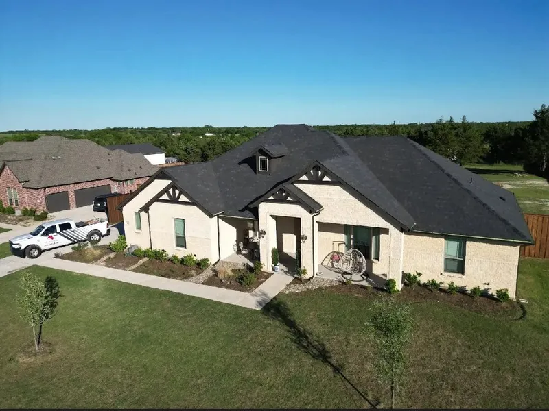 A white stone home with a new dark shingle roof and a Century Roofing truck in the drive